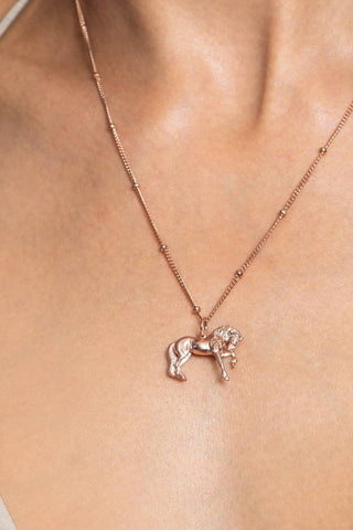 A person wearing a necklace with a pendant featuring a FRIESIAN horse design. A pendant in the shape of a horse, hanging from a gold chain. The FRIESIAN horse is depicted mid-stride with intricate details, including a flowing mane and tail. The chain features small, rounded beads spaced along its length. Ideal as a special equestrian gift for women, equestrians, horses and Friesian horses lovers. 