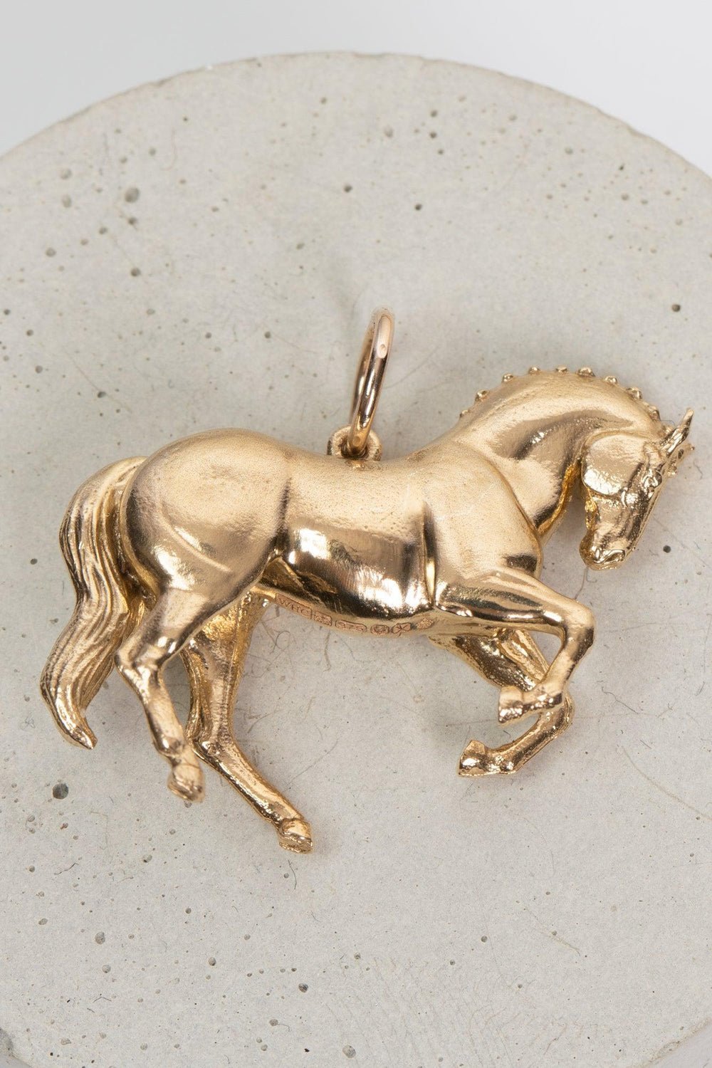 A gold horse pendant elegantly displayed, showcasing its intricate design and craftsmanship.The pendant is shaped like a  wild horse in mid-stride, with detailed features such as its mane and tail.  The background appears to be a plain or stone , light-colored surface.  Perfect for horse lovers, fans of equestrian inspired jewelry, horseback riders,  gold horse jewelry, unique equine gifts, horse girls. A dynamic piece of Horse Jewelry.