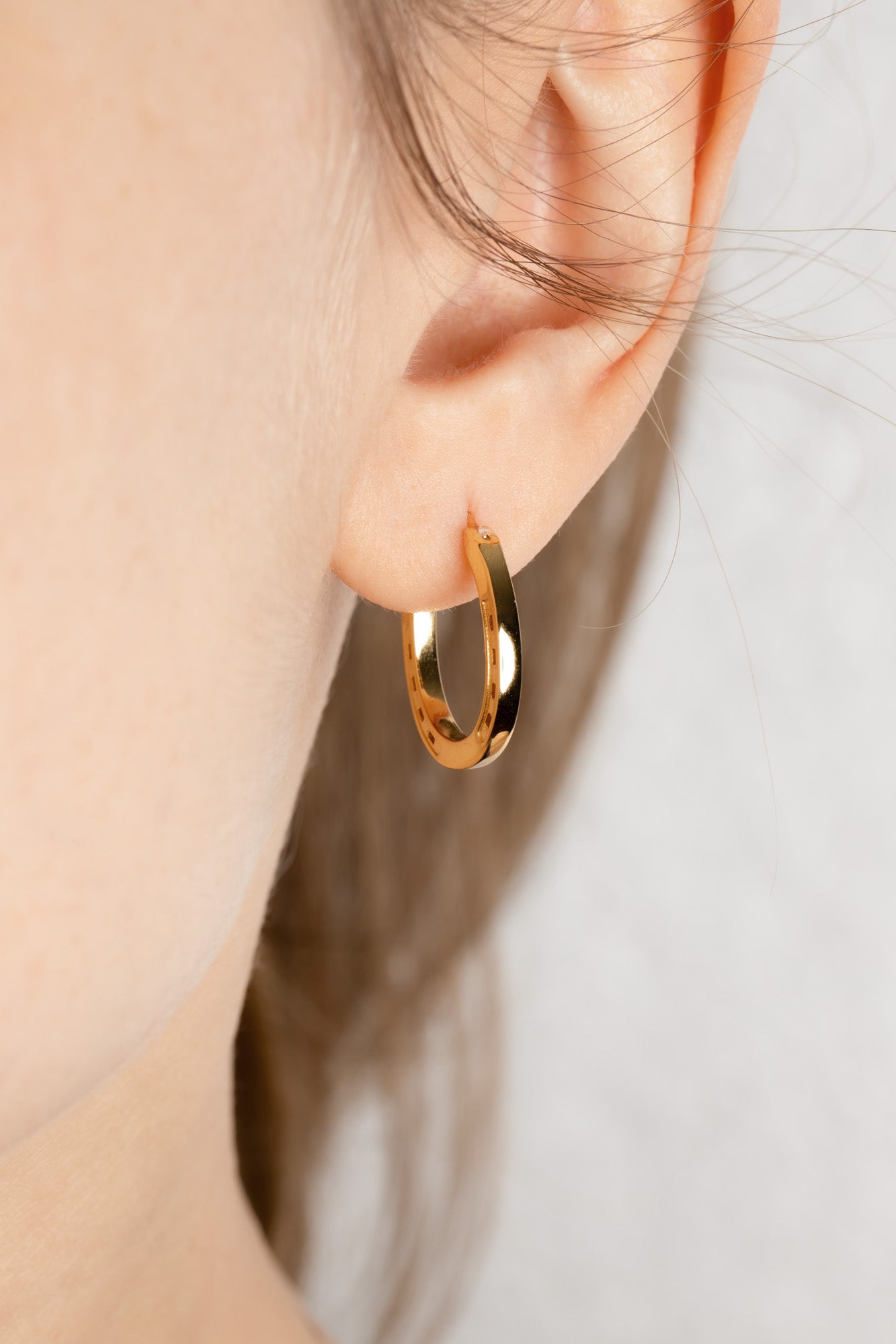 A close-up of a pair of elegant gold hoop horseshoe earrings on a blond model, emphasizing their gleaming finish and stylish form. Our Gold Horse Shoe Earrings are unique equestrian gifts crafted from high-quality gold. This gold horseshoe earrings are the perfect equestrian lifestyle fan gift and a good luck charm. Our Horseshoe earrings are the perfect birthday present for horse lovers, horse girls, cowgirls. A representation of good luck.