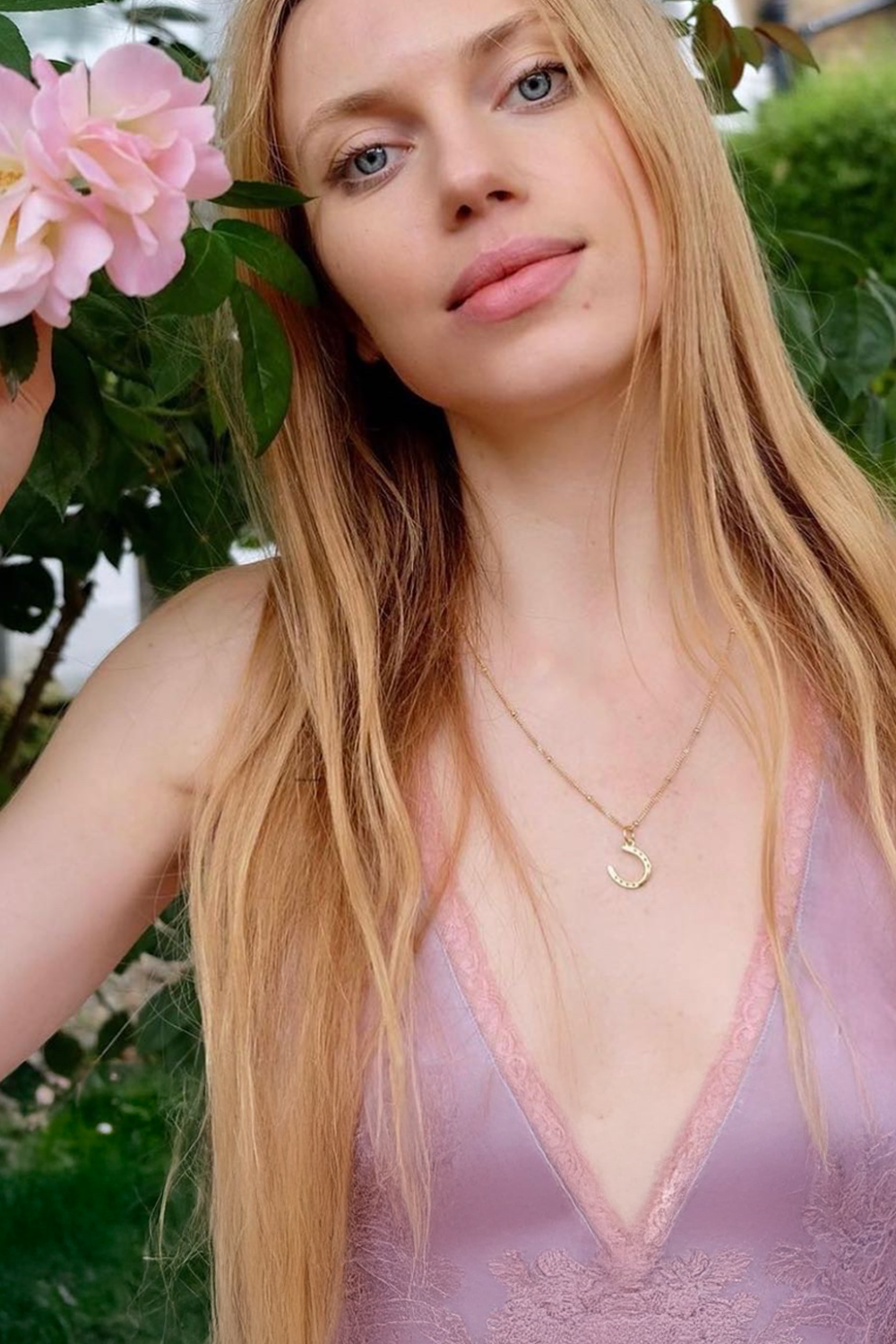 A blond  woman model displays a stylish horseshoe necklace, emphasizing personal style and sophistication. A Gold horseshoe necklace for luck. The necklace chain is also gold and has a series of small. Ideal as a unique gift, this pendant celebrates the beauty and strength of horses. Best gifts for horseback riders and one of a kind horse gift ideas for her. A unique horse gift and equestrian 