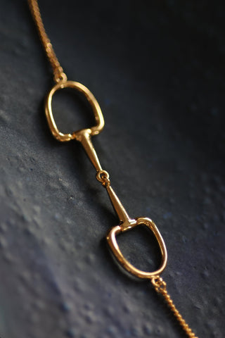 Close up of a stylish gold Snaffle Bit Necklace embodying sophistication in its design.  Perfect for horse enthusiasts and fashion lovers, it adds a refined touch to any outfit and makes a memorable equestrian gifts for women and horse themed gifts. Featuring a stunning snaffle bit pendant crafted from high-quality gold. 