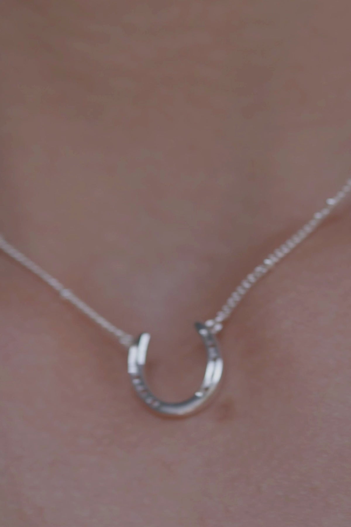 A silver necklace featuring a delicate horseshoe charm, symbolizing luck and elegance in a stylish design. 
The necklace chain is also silver  and has a series of small, rounded beads interspersed along its length with a heart at the end of the chain with engraved initials of WHC: Wild Horse Club. The background appears to be a light-colored surface stone. This horse shoe necklace is the perfect equestrian themed gift and as a good luck charm, horse lovers, silver girls.