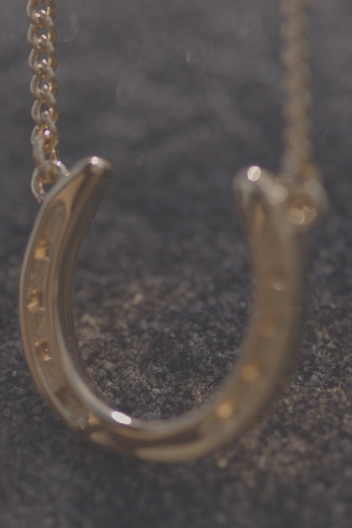  stylish gold necklace with a charming horseshoe pendant, embodying luck and refined beauty. The necklace chain is also gold and has a series of small, rounded beads interspersed along its length. The background appears to be a light-colored surface stone. This horse shoe necklace is the perfect equestrian themed gift and as a good luck charm, horse lovers.