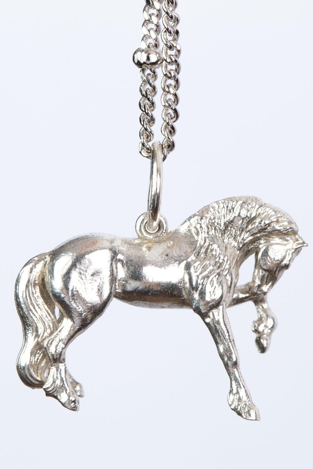 The Friesian Horse Pendant is a silver pendant in the shape of a horse, hanging from a silver chain. The FRIESIAN horse is depicted mid-stride with intricate details, including a flowing mane and tail. The chain features small, rounded beads spaced along its length. The background of the FRIESIAN horse pendant is plain and light-colored. Ideal as a special equestrian gift for women, equestrians, horses and Friesian horses lovers, silver girls.