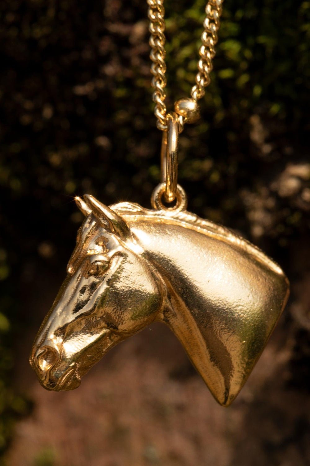A gold horse head necklace with detailed features such as its mane. The necklace chain is also gold and has a series of small, rounded beads interspersed along its length. The gold horse head pendant is elegantly displayed on a pristine white marble surface. Ideal as a unique gift, this pendant celebrates the beauty and strength of horses. Best gifts for horseback riders and one of a kind horse gift ideas for her.